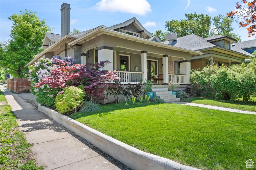 View of front of property with a porch, brick siding, a front yard, and a chimney