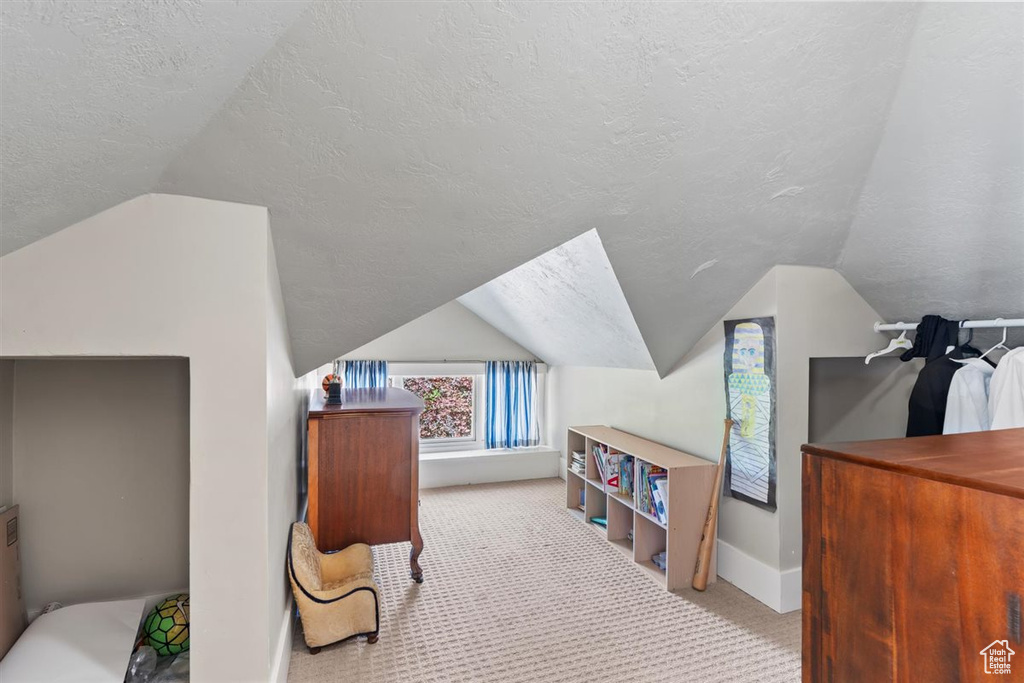 Bedroom featuring a textured ceiling, vaulted ceiling, baseboards, and carpet