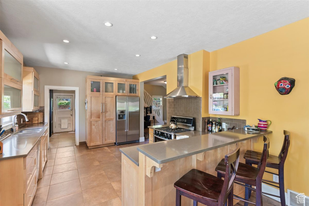 Kitchen with wall chimney range hood, appliances with stainless steel finishes, a sink, and tasteful backsplash