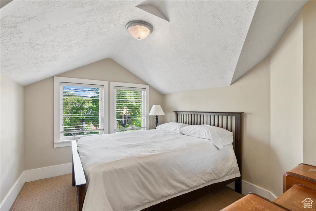 Carpeted bedroom featuring baseboards, a textured ceiling, and lofted ceiling