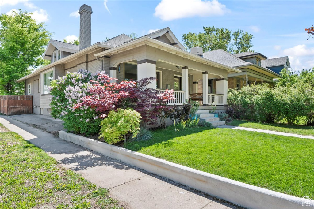 View of front of house with a porch, a chimney, brick siding, fence, and a front lawn