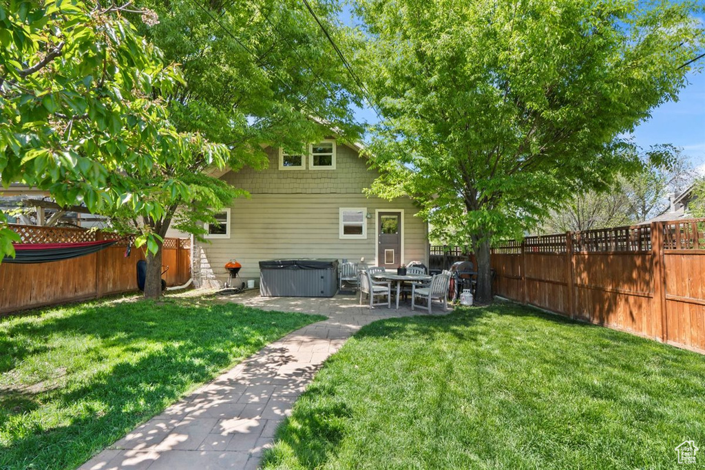 Back of property featuring a lawn, a fenced backyard, a hot tub, and a patio area