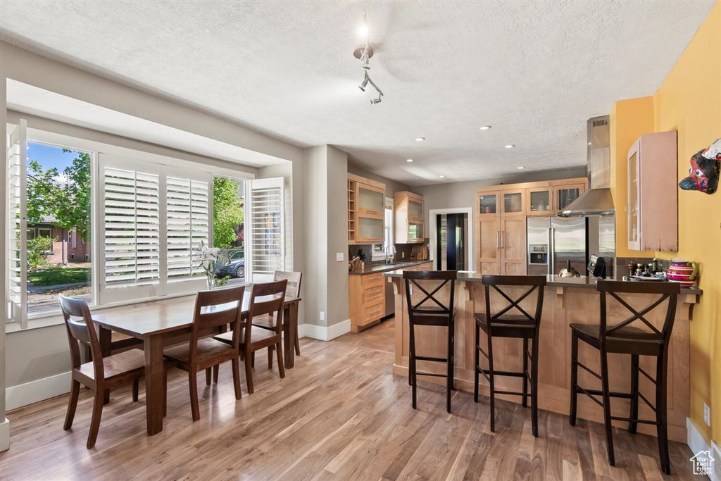 Kitchen with a peninsula, dark countertops, wall chimney range hood, a textured ceiling, and appliances with stainless steel finishes