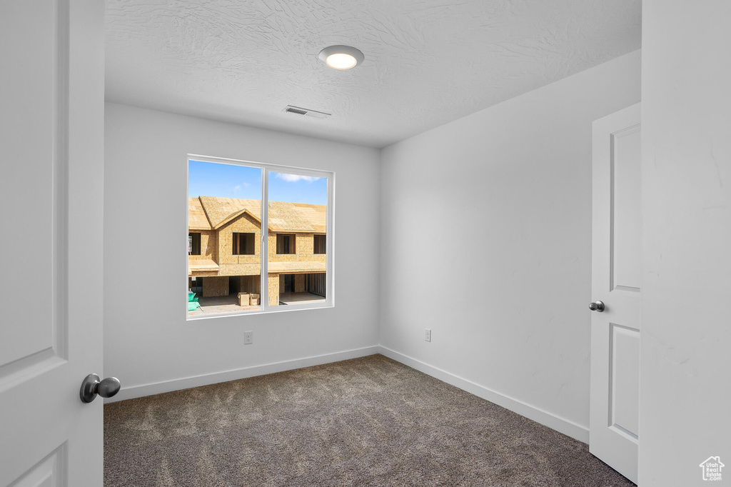 Spare room with carpet flooring, a textured ceiling, visible vents, and baseboards
