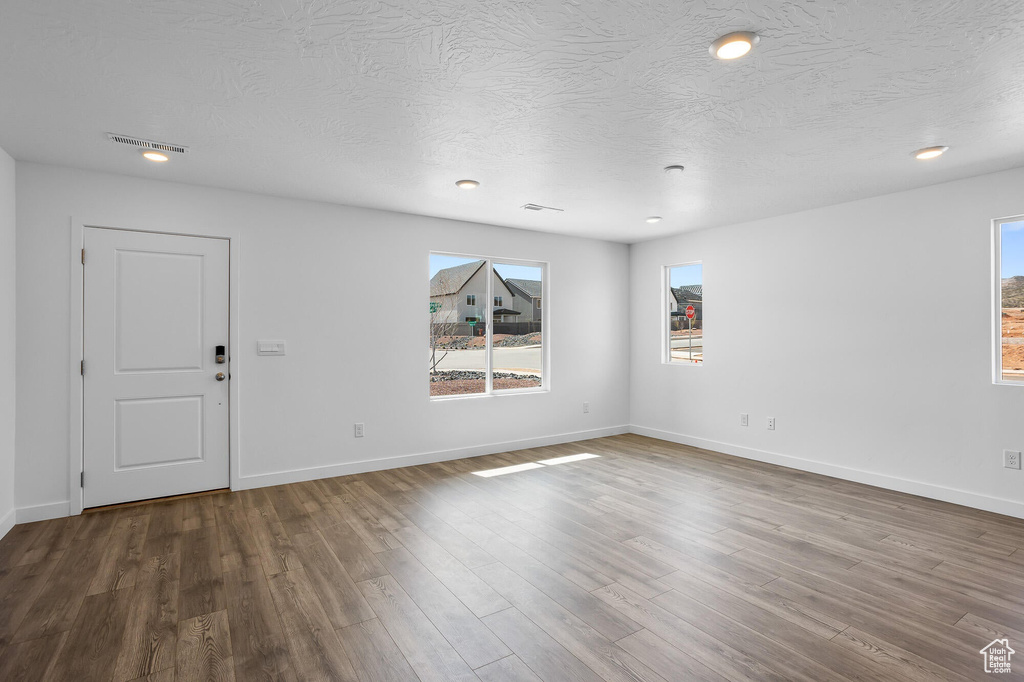 Unfurnished living room featuring a textured ceiling, baseboards, and wood finished floors