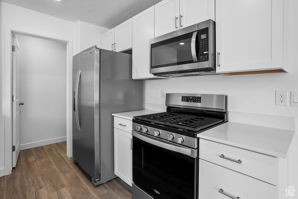 Kitchen with stainless steel appliances, white cabinetry, light countertops, and dark wood-type flooring