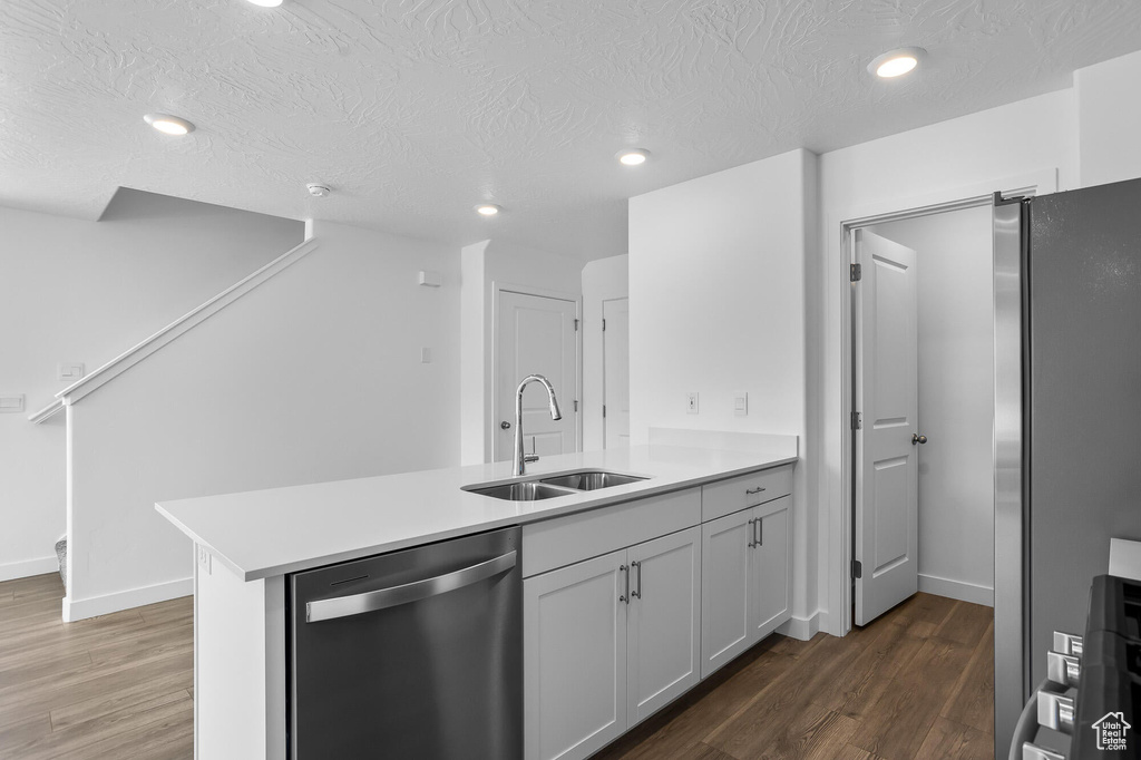 Kitchen featuring stainless steel appliances, a sink, a peninsula, wood finished floors, and light countertops