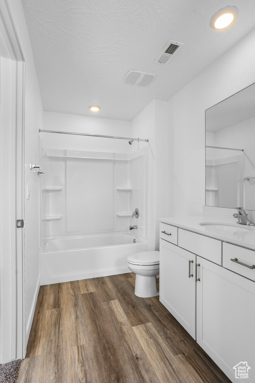 Bathroom featuring toilet, wood finished floors, shower / tub combination, visible vents, and vanity