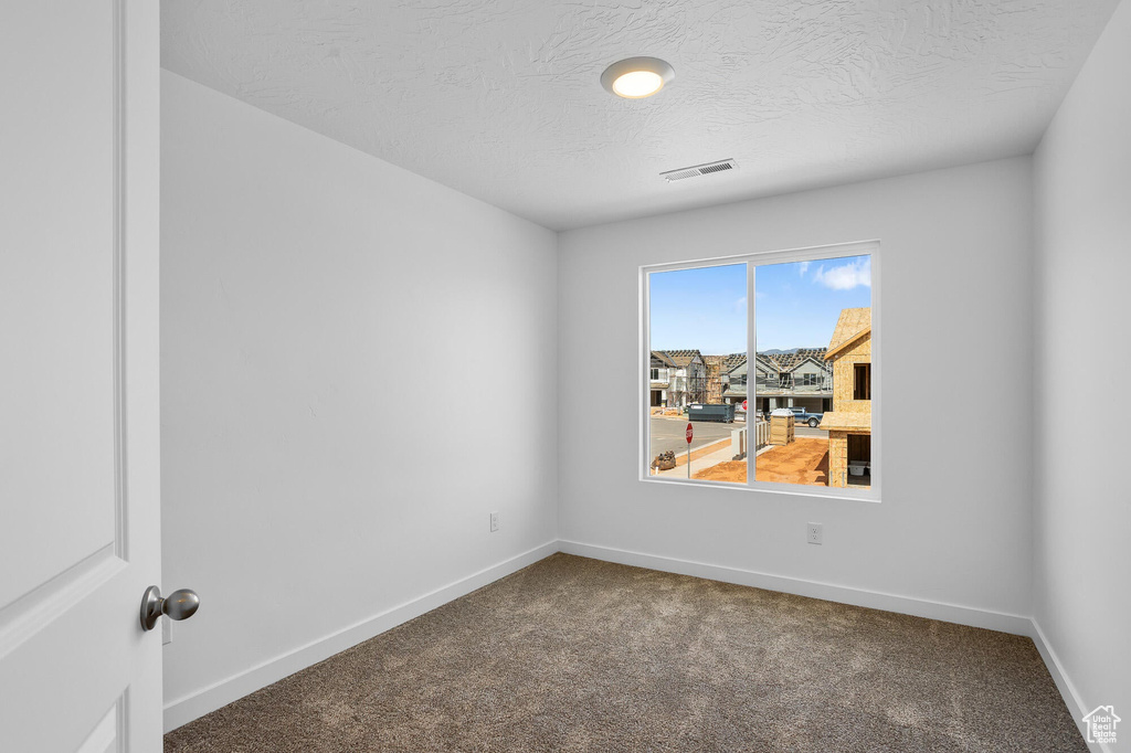 Empty room featuring baseboards, carpet flooring, visible vents, and a textured ceiling