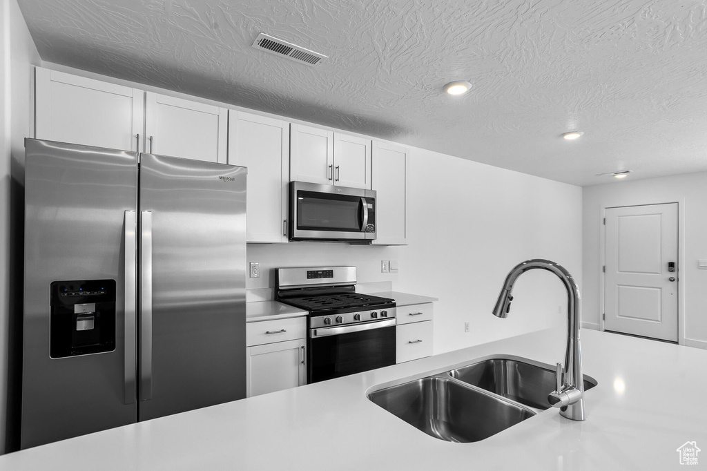 Kitchen featuring a sink, stainless steel appliances, visible vents, white cabinetry, and light countertops
