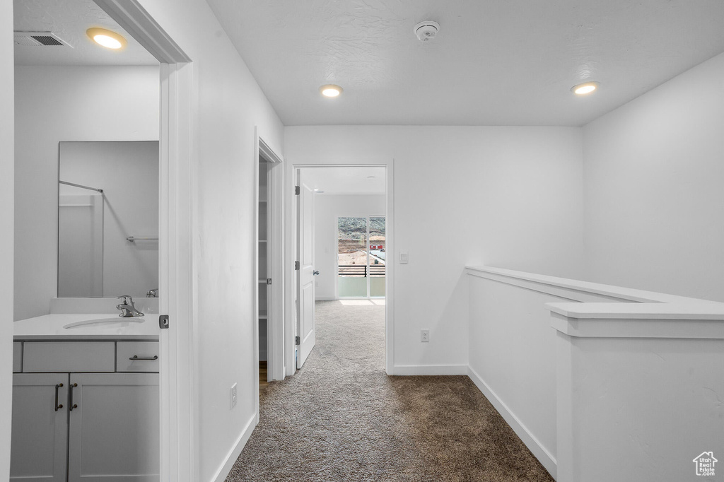 Corridor with a sink, visible vents, recessed lighting, dark colored carpet, and baseboards