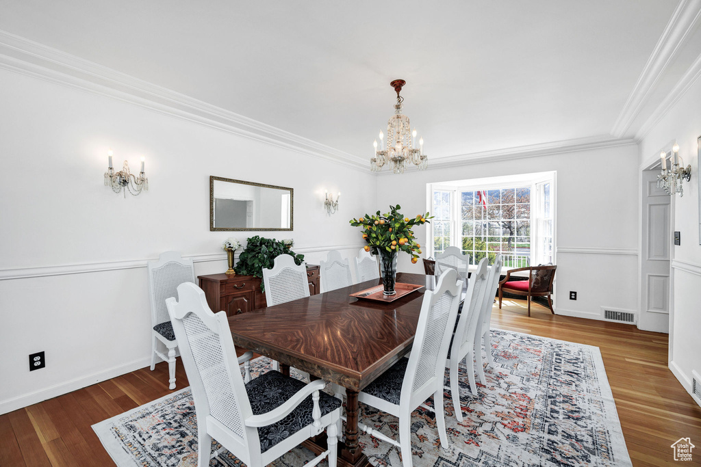 Dining room featuring wood finished floors, crown molding, visible vents, baseboards, and a chandelier