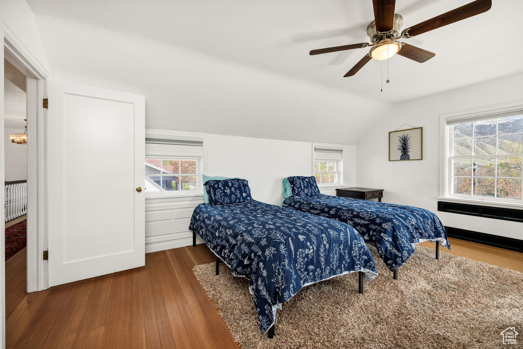 Bedroom featuring lofted ceiling, radiator heating unit, ceiling fan, and wood finished floors