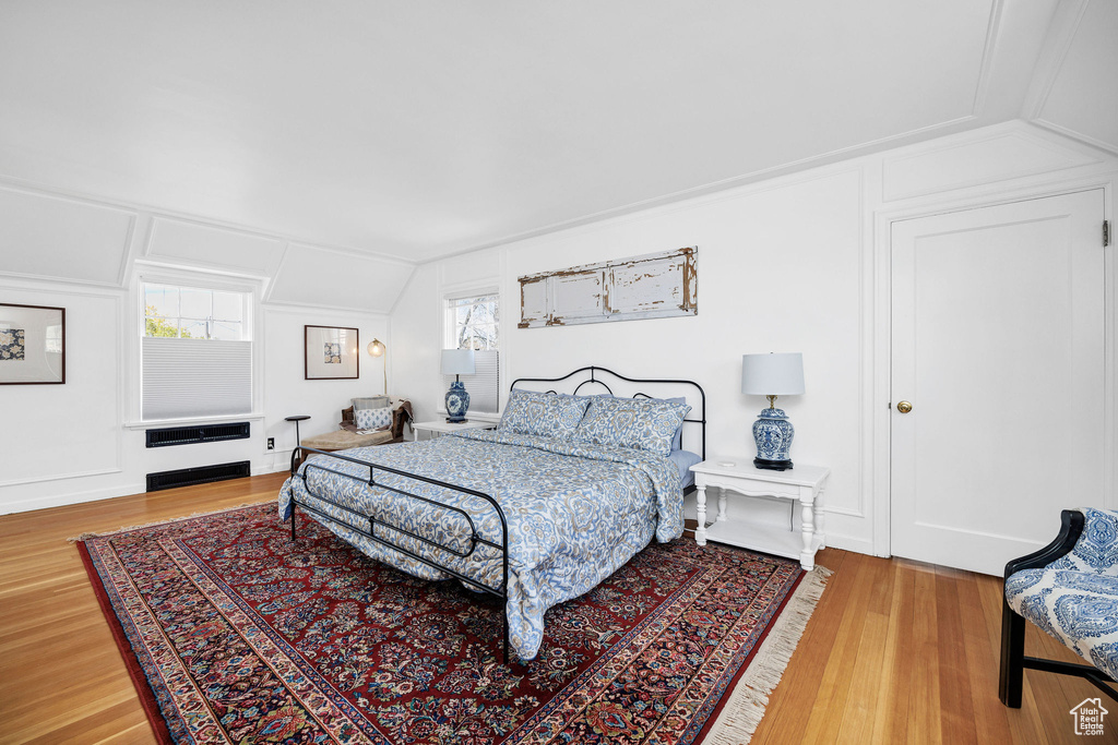Bedroom with a decorative wall, wood finished floors, and lofted ceiling