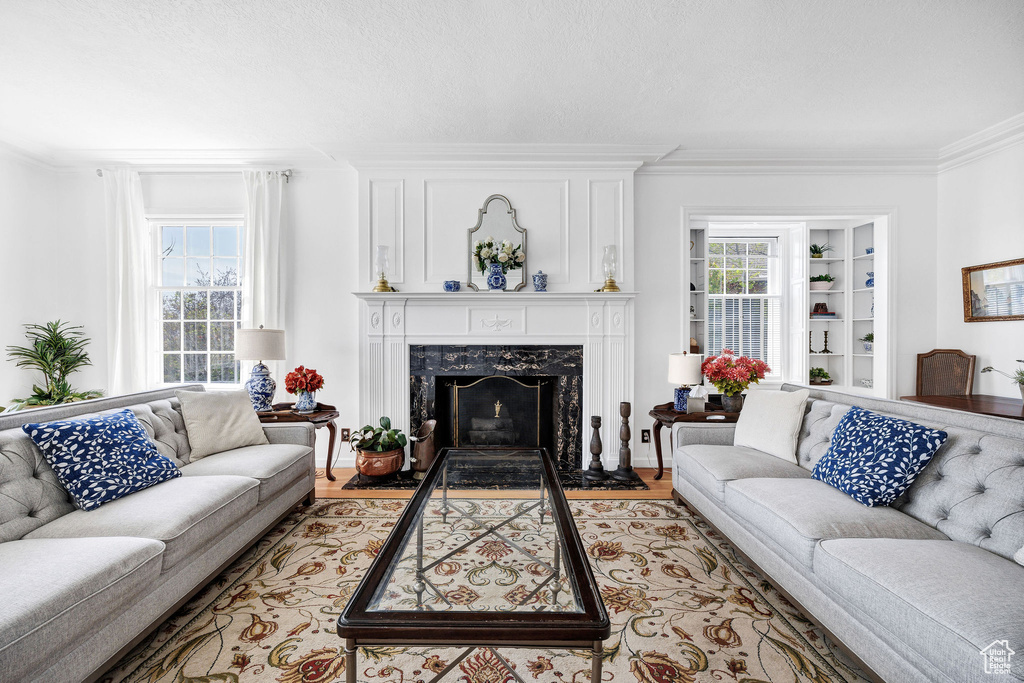 Living room with built in shelves, ornamental molding, a high end fireplace, and light wood-style floors