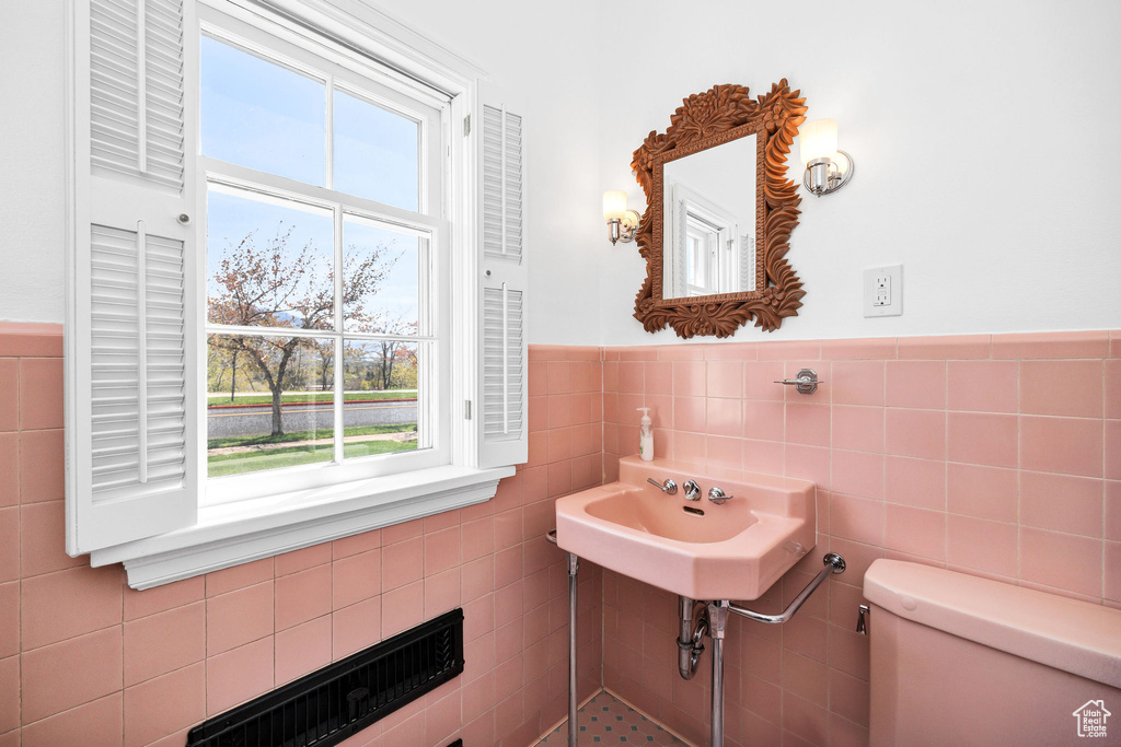 Bathroom featuring toilet, tile walls, a wainscoted wall, and plenty of natural light