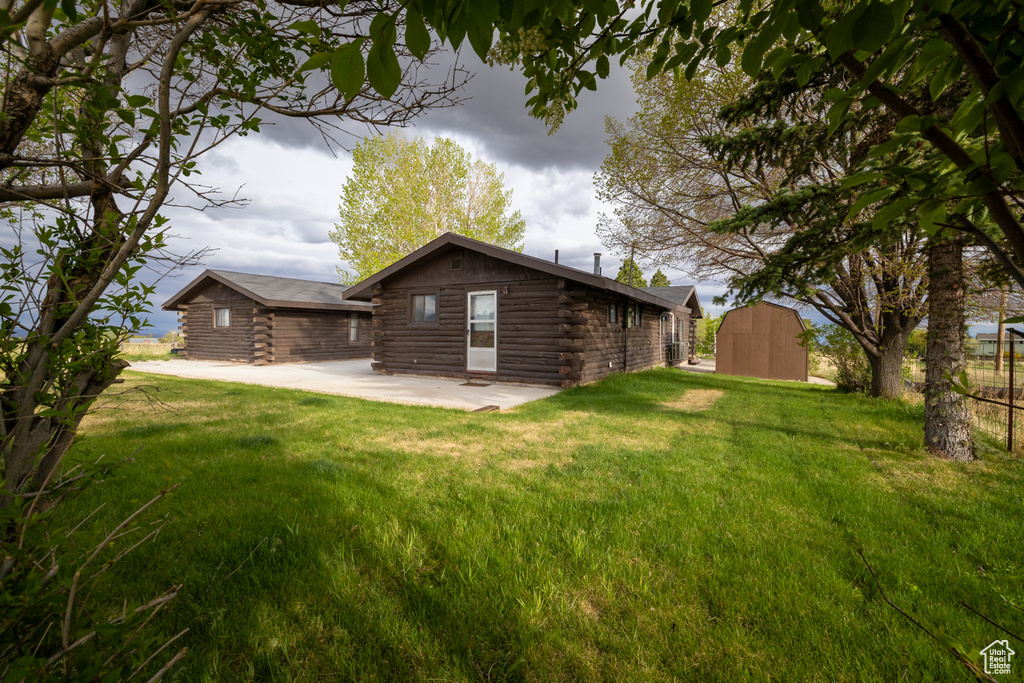 Rear view of property with log siding, a lawn, a patio, and an outbuilding