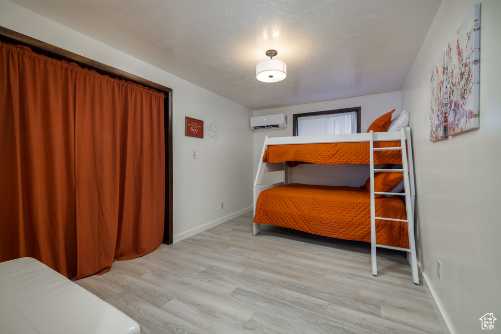 Bedroom with a wall mounted AC, wood finished floors, and baseboards