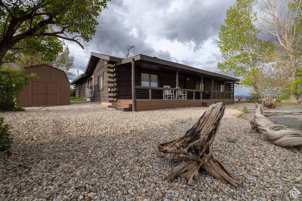 View of front of home featuring log exterior, a shed, an outdoor structure, and covered porch