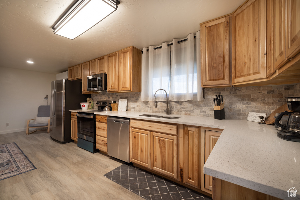 Kitchen with appliances with stainless steel finishes, a sink, decorative backsplash, light wood-style flooring, and baseboards
