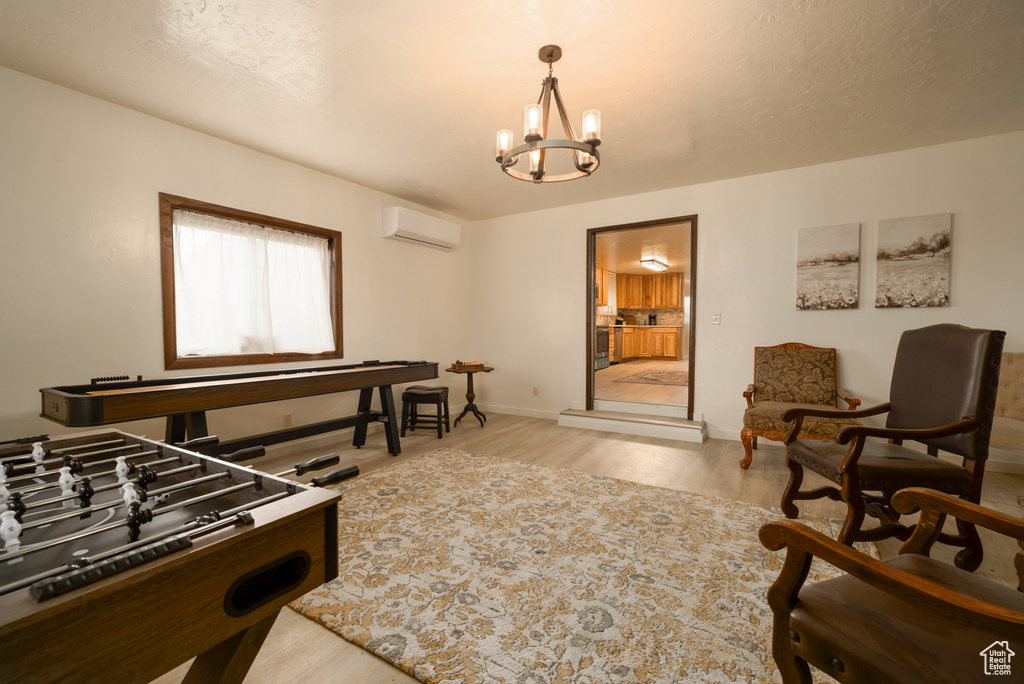 Recreation room featuring an AC wall unit, a chandelier, light wood-style flooring, and baseboards