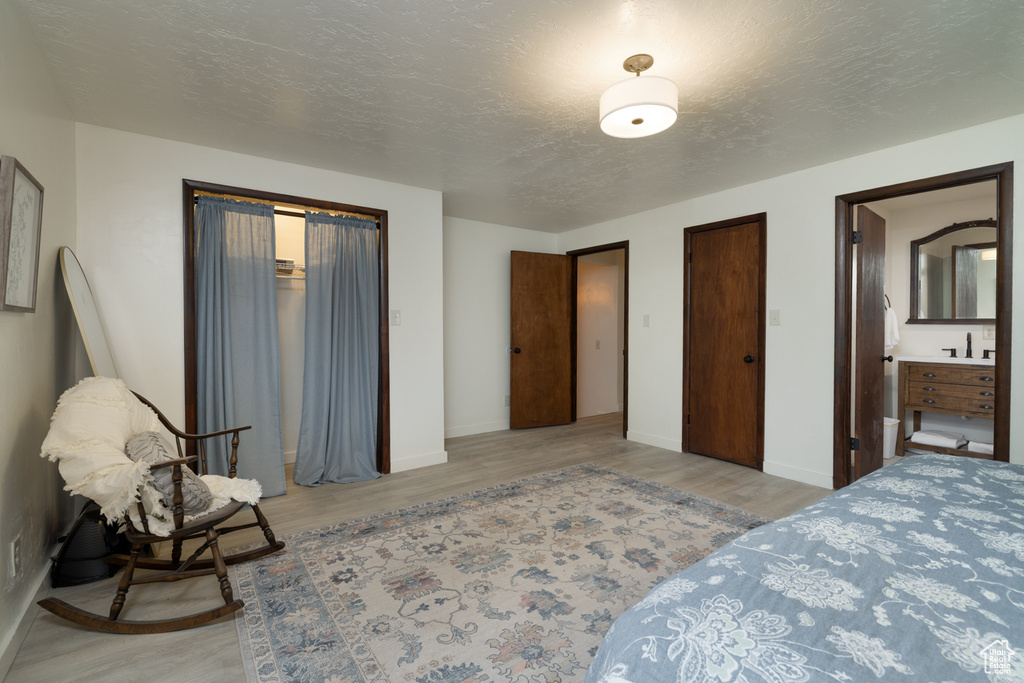 Bedroom with light wood finished floors, baseboards, and a textured ceiling