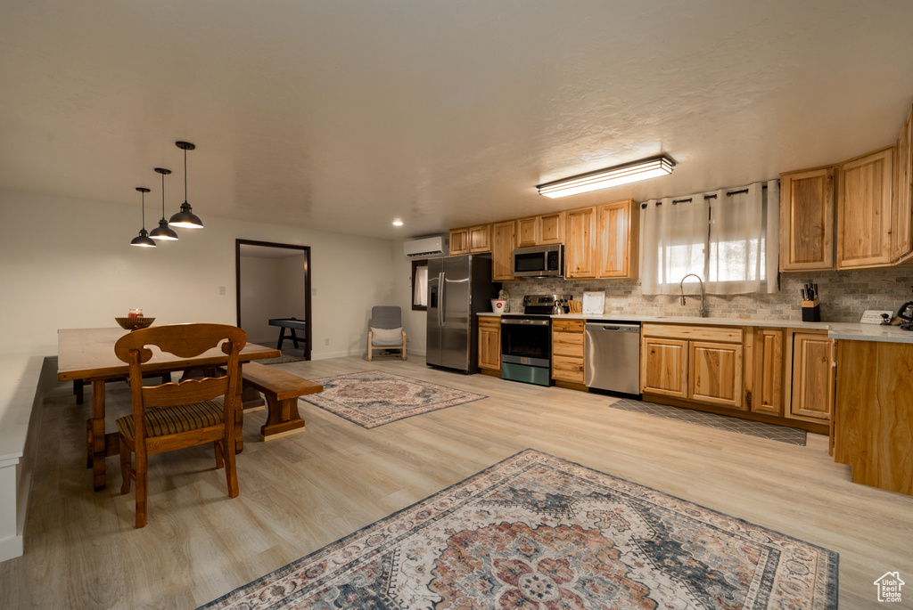 Kitchen featuring stainless steel appliances, a wall mounted air conditioner, light wood-style floors, light countertops, and decorative backsplash