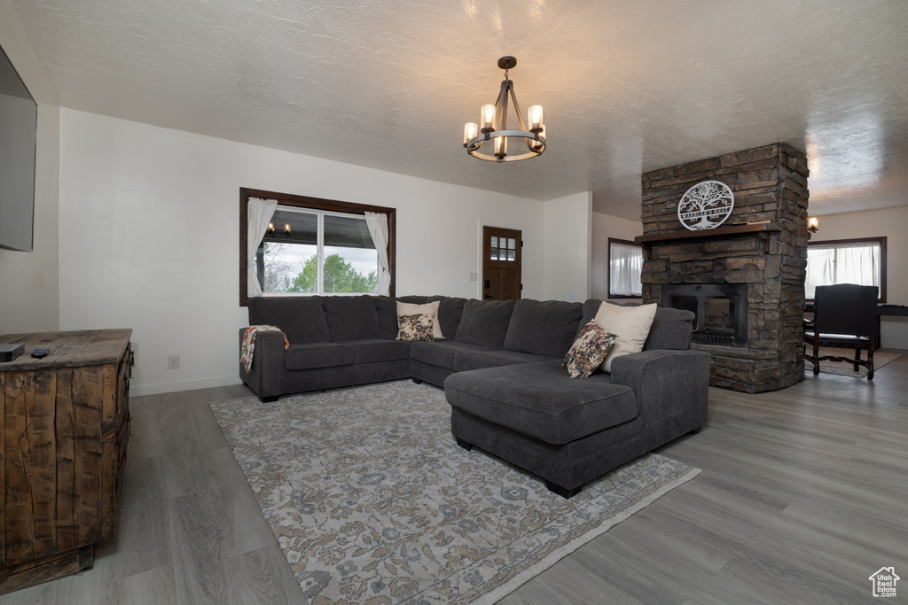 Living area with wood finished floors, a chandelier, baseboards, and a stone fireplace