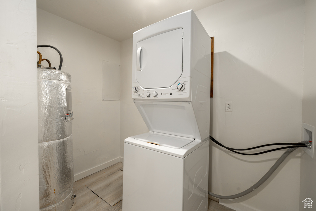 Washroom featuring stacked washing machine and dryer, light wood-style flooring, water heater, and baseboards