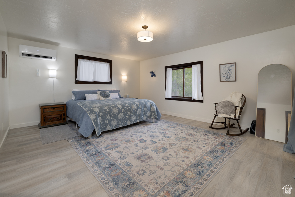 Bedroom featuring a wall unit AC, light wood finished floors, baseboards, and arched walkways