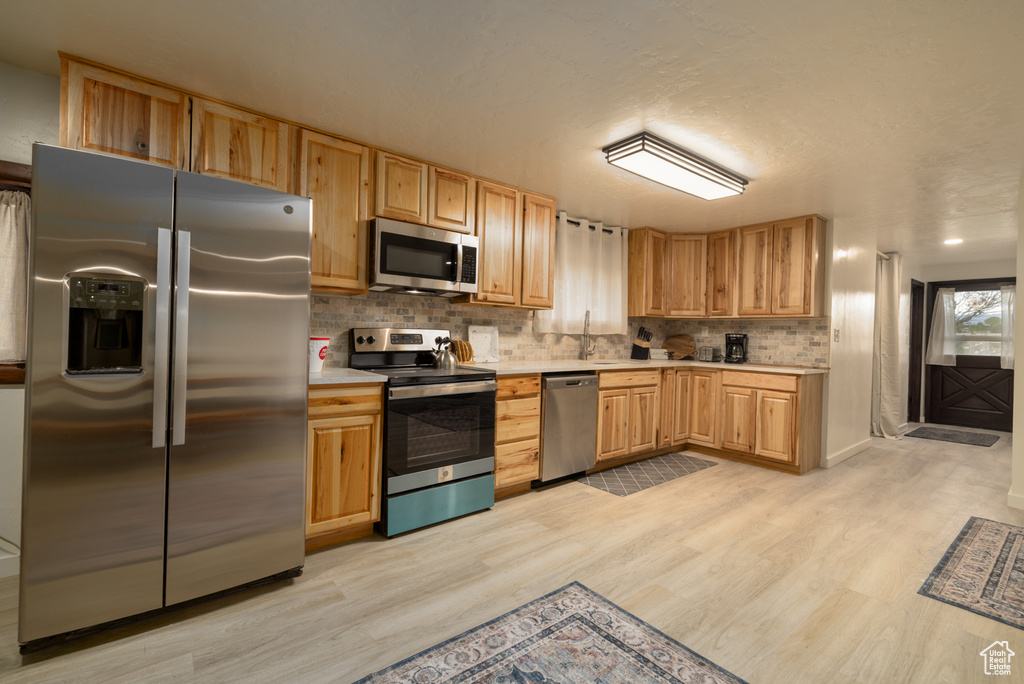 Kitchen featuring stainless steel appliances, light countertops, light wood finished floors, and tasteful backsplash