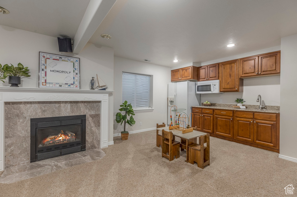 Kitchen with baseboards, white appliances, a tiled fireplace, brown cabinets, and light colored carpet