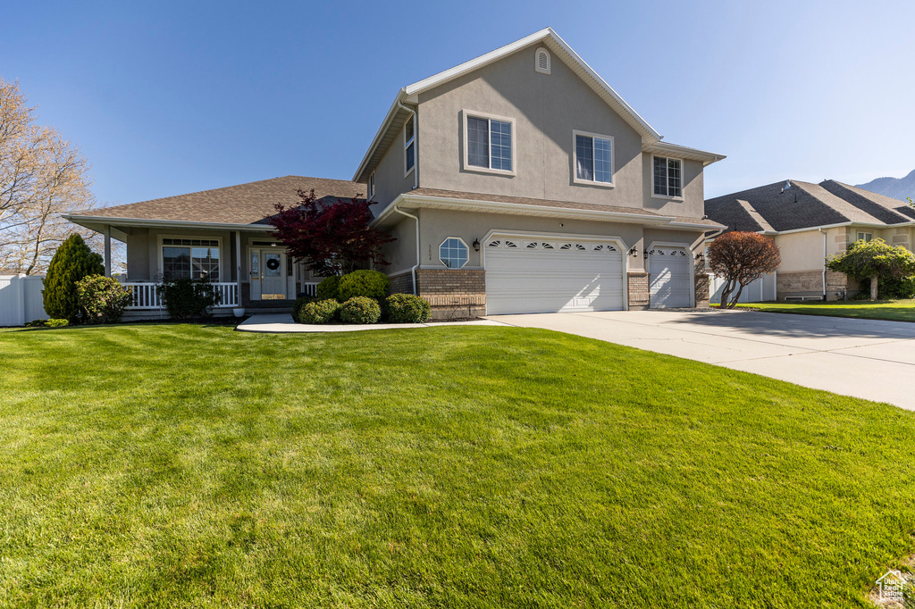 Traditional home with a garage, concrete driveway, a porch, a front yard, and brick siding