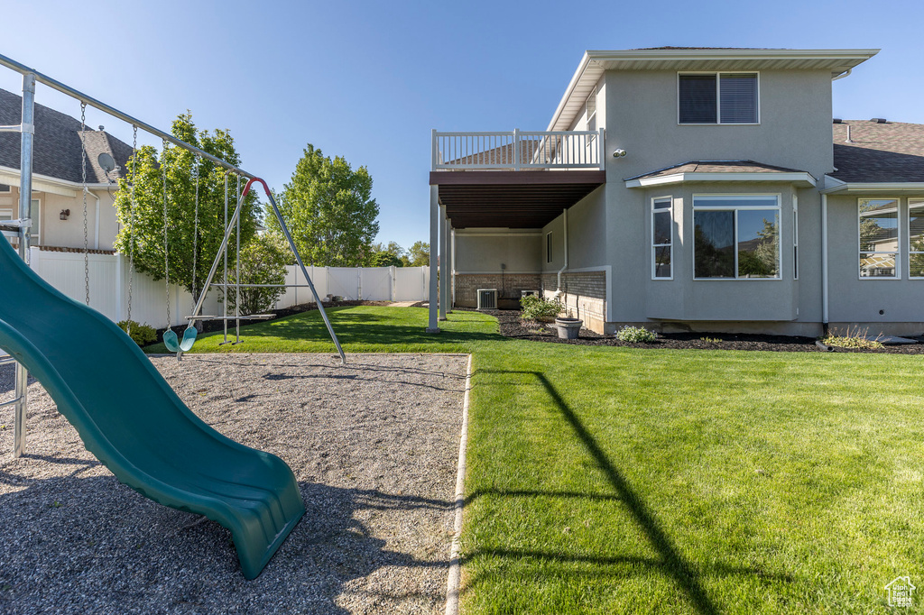 Back of house featuring a balcony, a yard, stucco siding, a fenced backyard, and playground community
