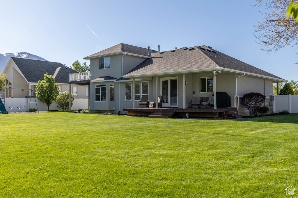 Rear view of house featuring a yard, a wooden deck, stucco siding, and fence