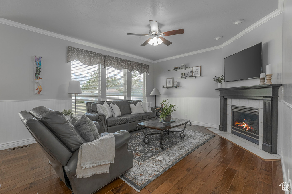 Living room featuring ornamental molding, a tile fireplace, ceiling fan, and a wainscoted wall