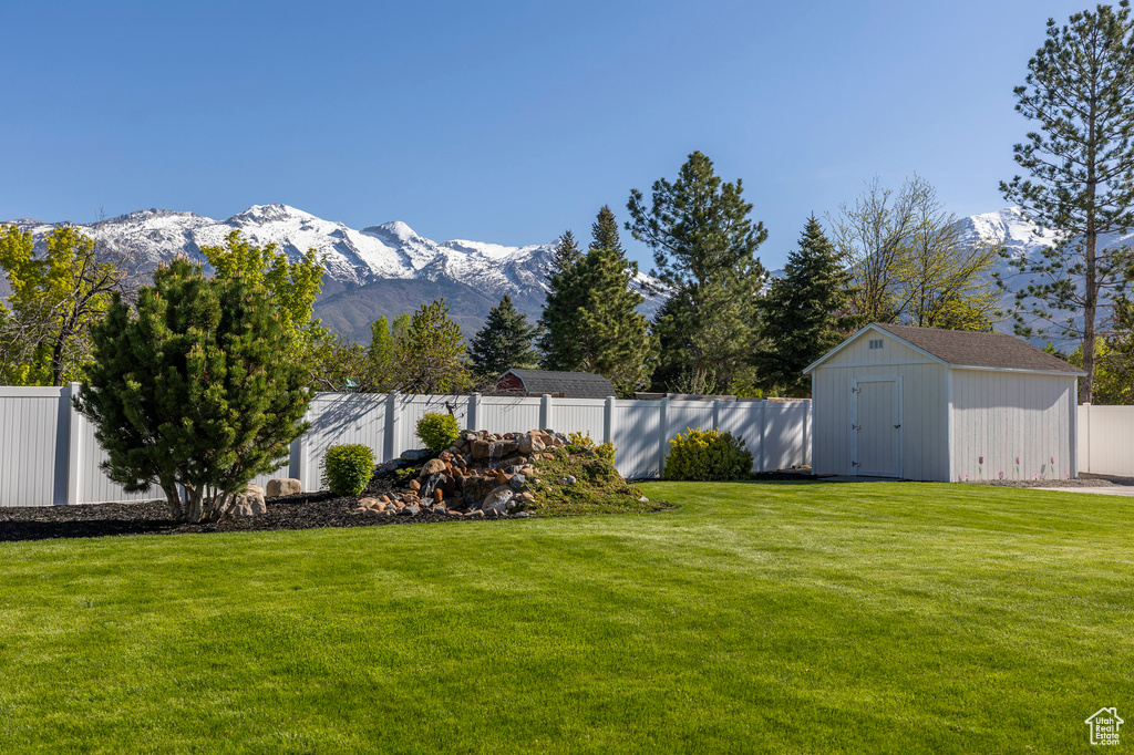 View of yard with a fenced backyard, a storage shed, a mountain view, and an outbuilding