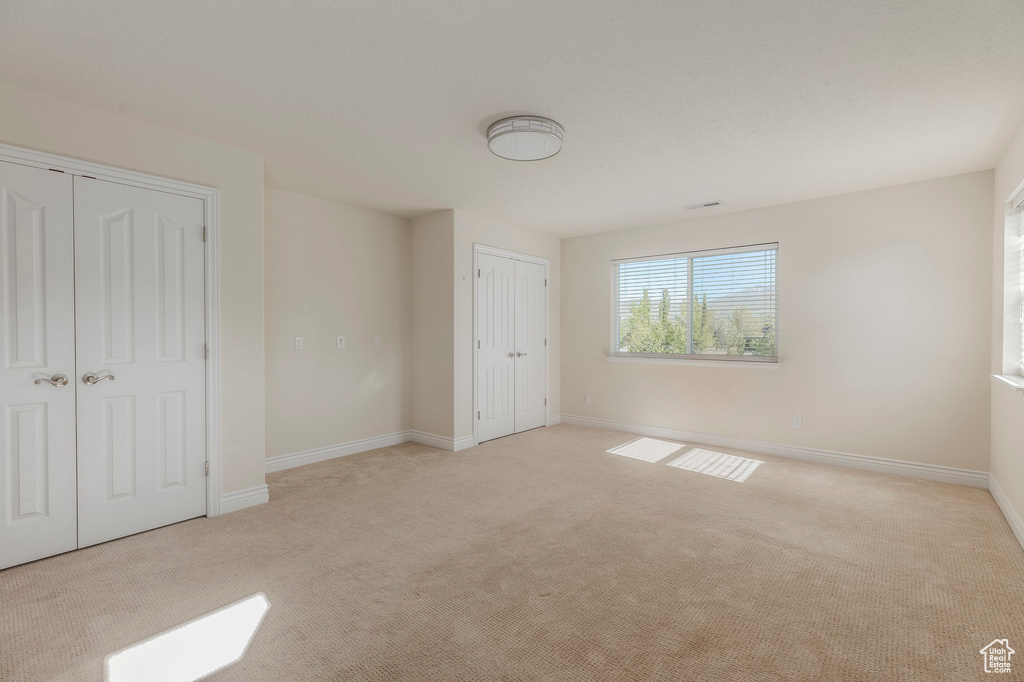 Unfurnished bedroom with light carpet, baseboards, and multiple closets