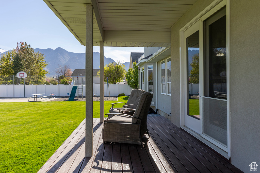 Wooden deck featuring fence, a playground, a mountain view, and a lawn
