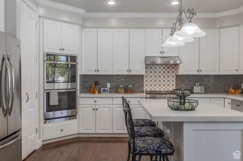 Kitchen featuring stainless steel appliances, under cabinet range hood, white cabinetry, crown molding, and light countertops