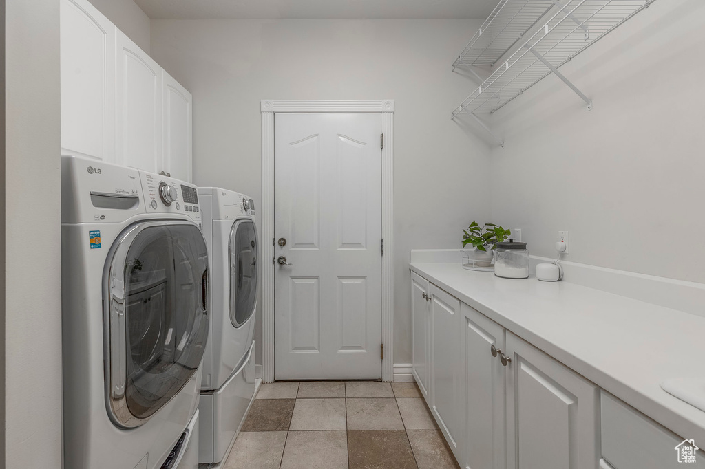 Clothes washing area featuring cabinet space, washing machine and clothes dryer, and light tile patterned flooring