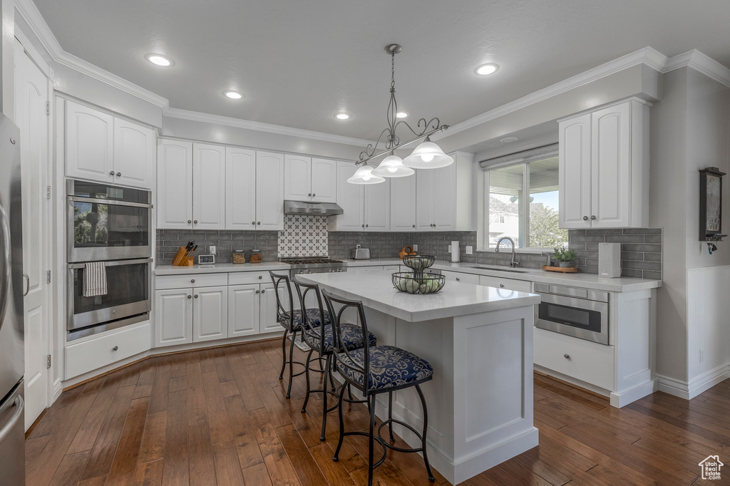Kitchen featuring a kitchen bar, white cabinets, under cabinet range hood, light countertops, and appliances with stainless steel finishes