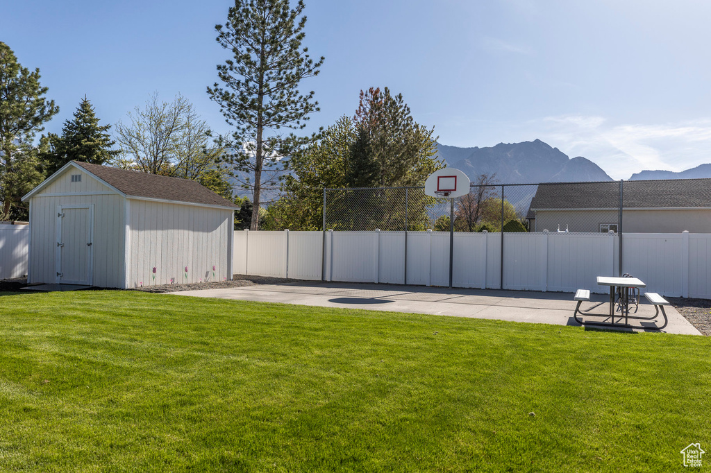 View of yard with an outbuilding, a mountain view, fence, a shed, and basketball court
