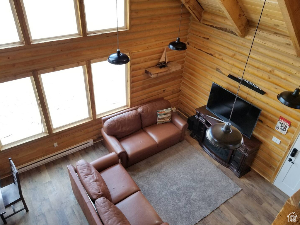 Living area featuring a baseboard radiator, beam ceiling, rustic walls, and wood finished floors