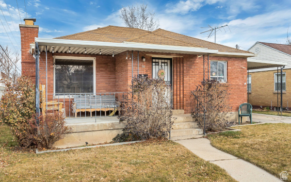 Bungalow-style home with a chimney, covered porch, and a front lawn