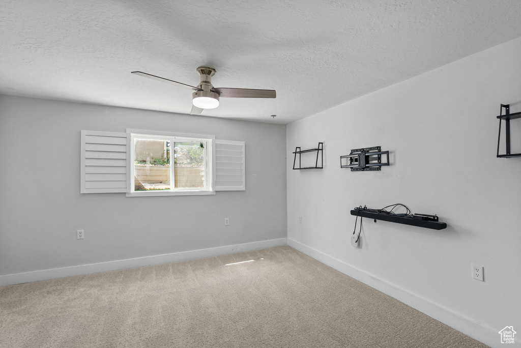 Carpeted spare room with a ceiling fan, baseboards, and a textured ceiling