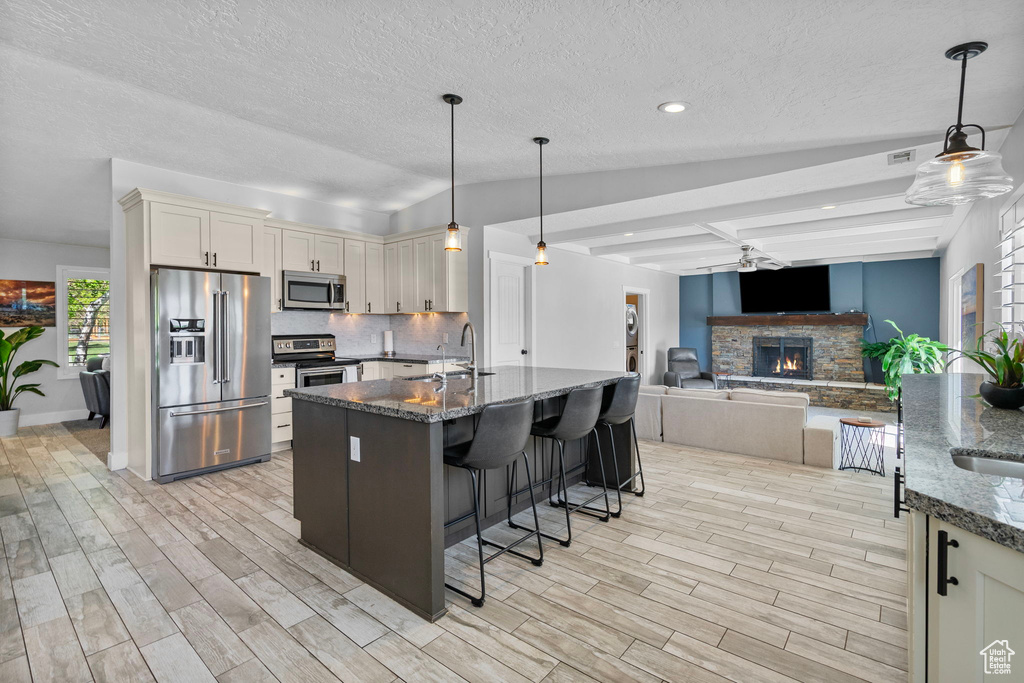 Kitchen featuring a breakfast bar area, a sink, dark stone countertops, backsplash, and appliances with stainless steel finishes