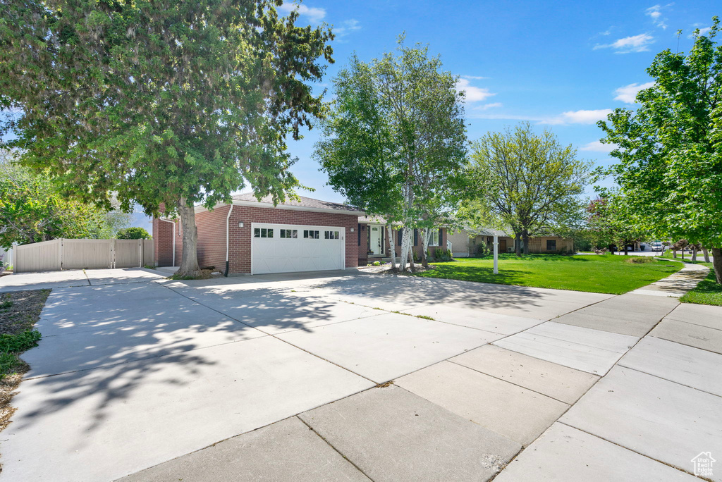 View of front of property with driveway, brick siding, fence, a garage, and a front yard