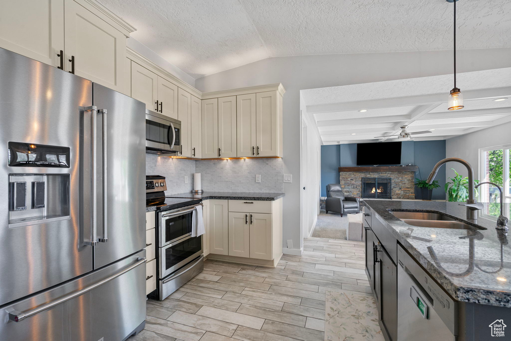 Kitchen with a sink, stainless steel appliances, a stone fireplace, ceiling fan, and tasteful backsplash