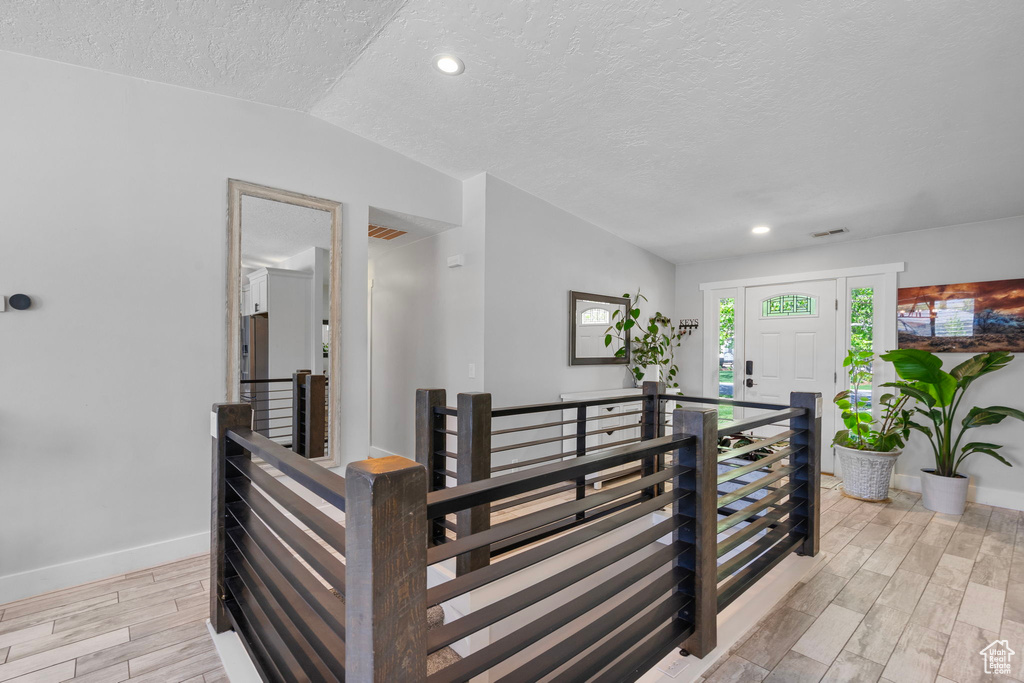 Corridor featuring a textured ceiling, an upstairs landing, baseboards, and light wood-style floors
